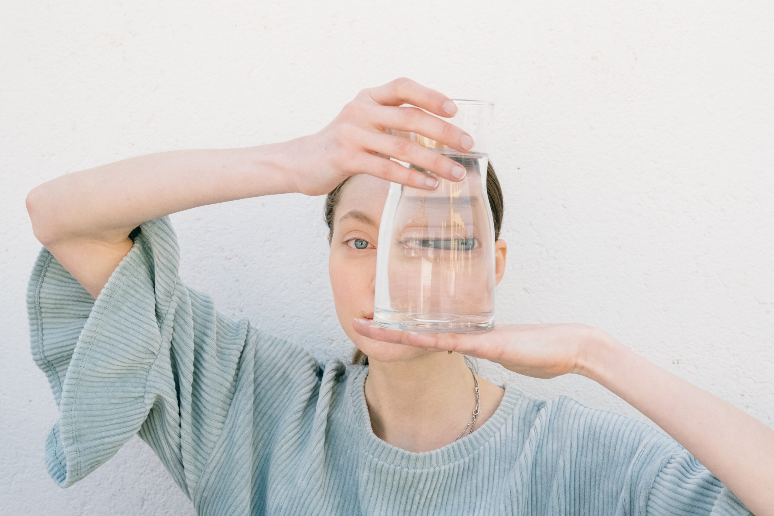 Kobieta na bliskim planie trzymająca szklany wazon wypełniony wodą przy twarzy